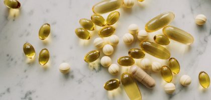 A variety of capsules and pills scattered on a light marble background.